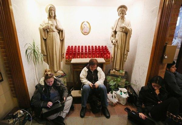 Ľudia odpočívajú a nabíjajú zariadenia v útulku pre tých, ktorých postihla Superstorm Sandy v kostole svätých Petra a Pavla 1. novembra 2012 v Hoboken v New Jersey.