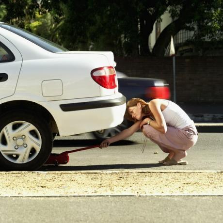 Vrouw staat op het punt auto op te tillen met hydraulische krik